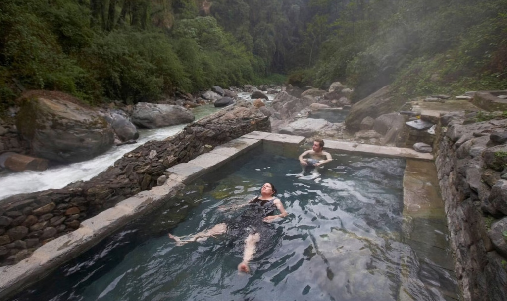 Trekkers soaking in natural stone thermal pools at Jhinu Danda next to a river
